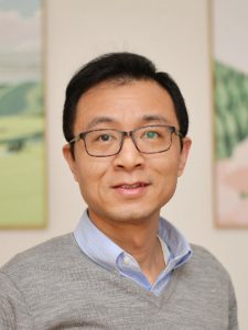 Asian man with short black hair wearing glasses and a gray sweater